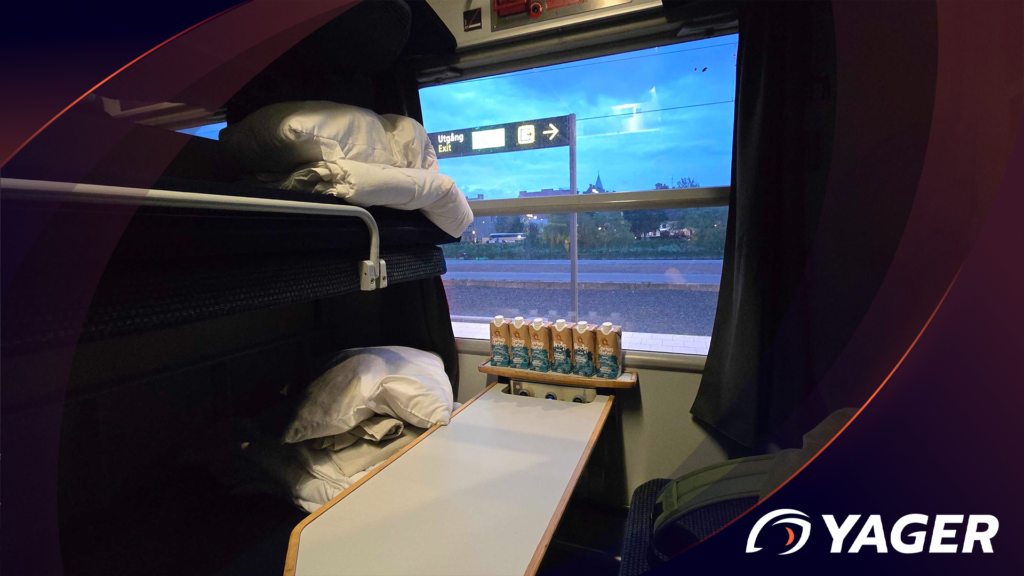 A table in a train sleeping cabin with some water. on the sides there are the bunk beds with bed sheets and pillows